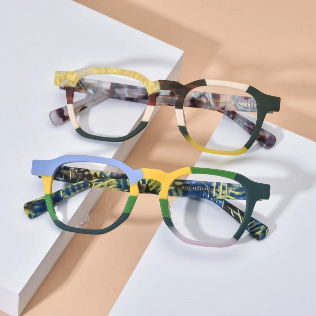 Lifestyle flatlay image showcasing VoyueLens™ VL19358 colorblock square glasses in both Citrus Fade and Ocean Tortoiseshell variants, styled on a soft neutral background to highlight vibrant frame contrasts and artistic acetate detailing.