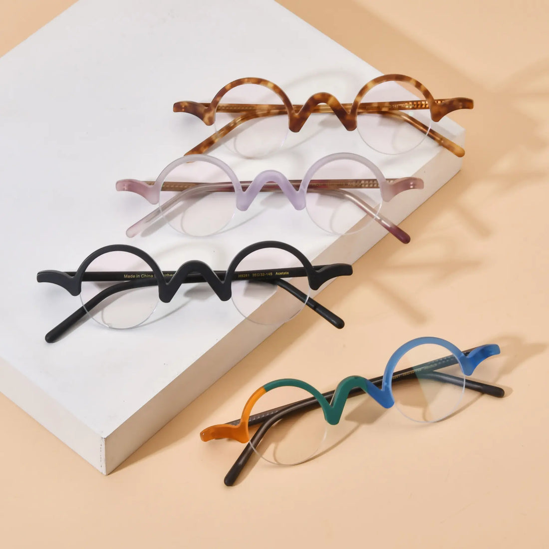 Group display of VoyueLens™ semi-rimless browline eyeglasses featuring Tortoiseshell, Lilac-Rose, Solid Black, and Teal-Blue color variants on beige background, highlighting wave top design and matte acetate frames.