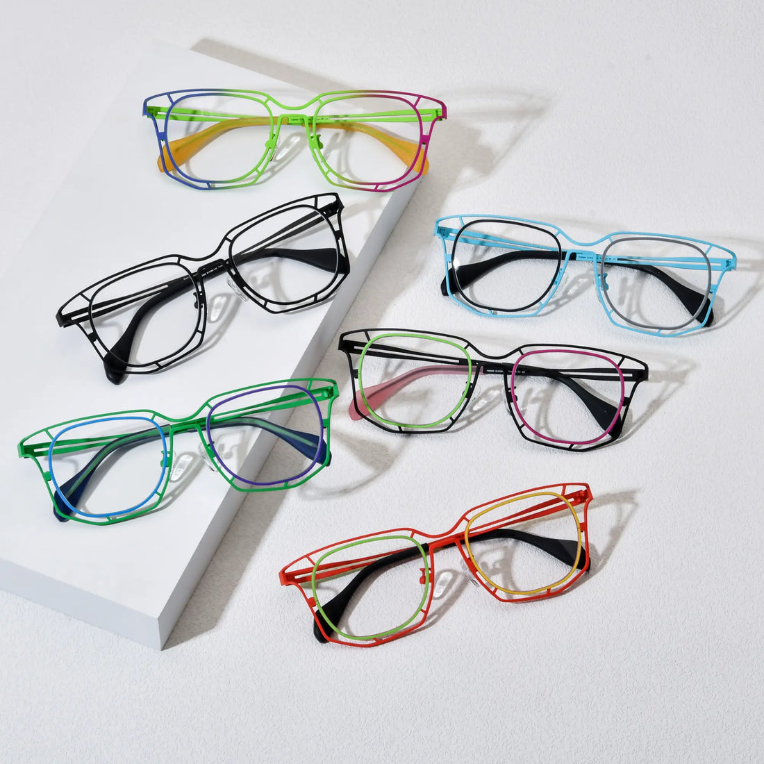 Display of VoyueLens™ VL185865 eyeglasses in six color variants – Rainbow Burst, Sky Blue, Graphite Black, Mint Pink Fusion, Emerald Twilight, and Amber Blaze. Polygonal titanium frames arranged on a textured background.
