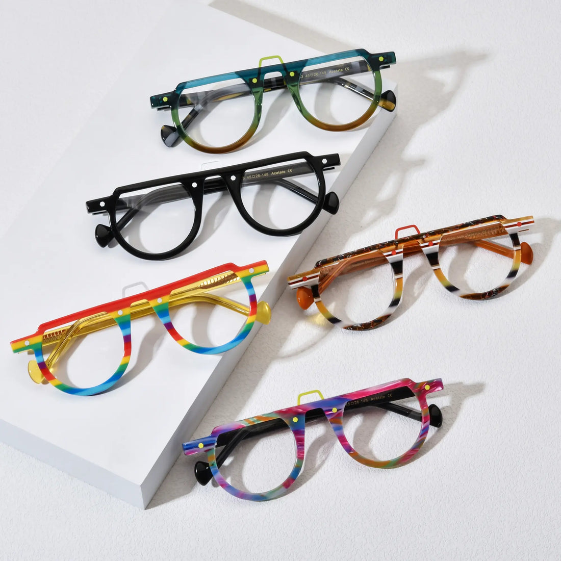 Top-down view of five VoyueLens™ VL19383 round eyeglass variants laid out on a white background, showcasing color options including Lime Tortoiseshell, Charcoal Black, Rainbow Stripe, Amber Stripe, and Rainbow Rush