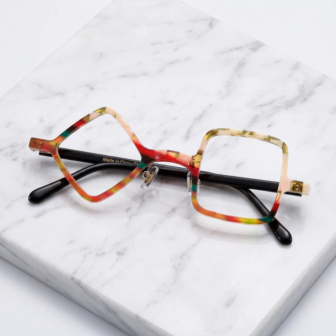 Barledear Amber Mosaic asymmetric geometric acetate eyeglasses folded display showing the warm patterned front, adjustable nose pads, and black temples.