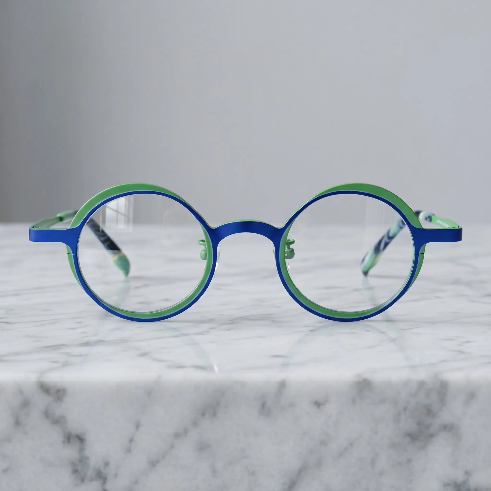 Barledear Cobalt Jade round titanium eyeglasses displayed in a clean lifestyle scene showing the artistic color-block design in vivid cobalt blue and jade green