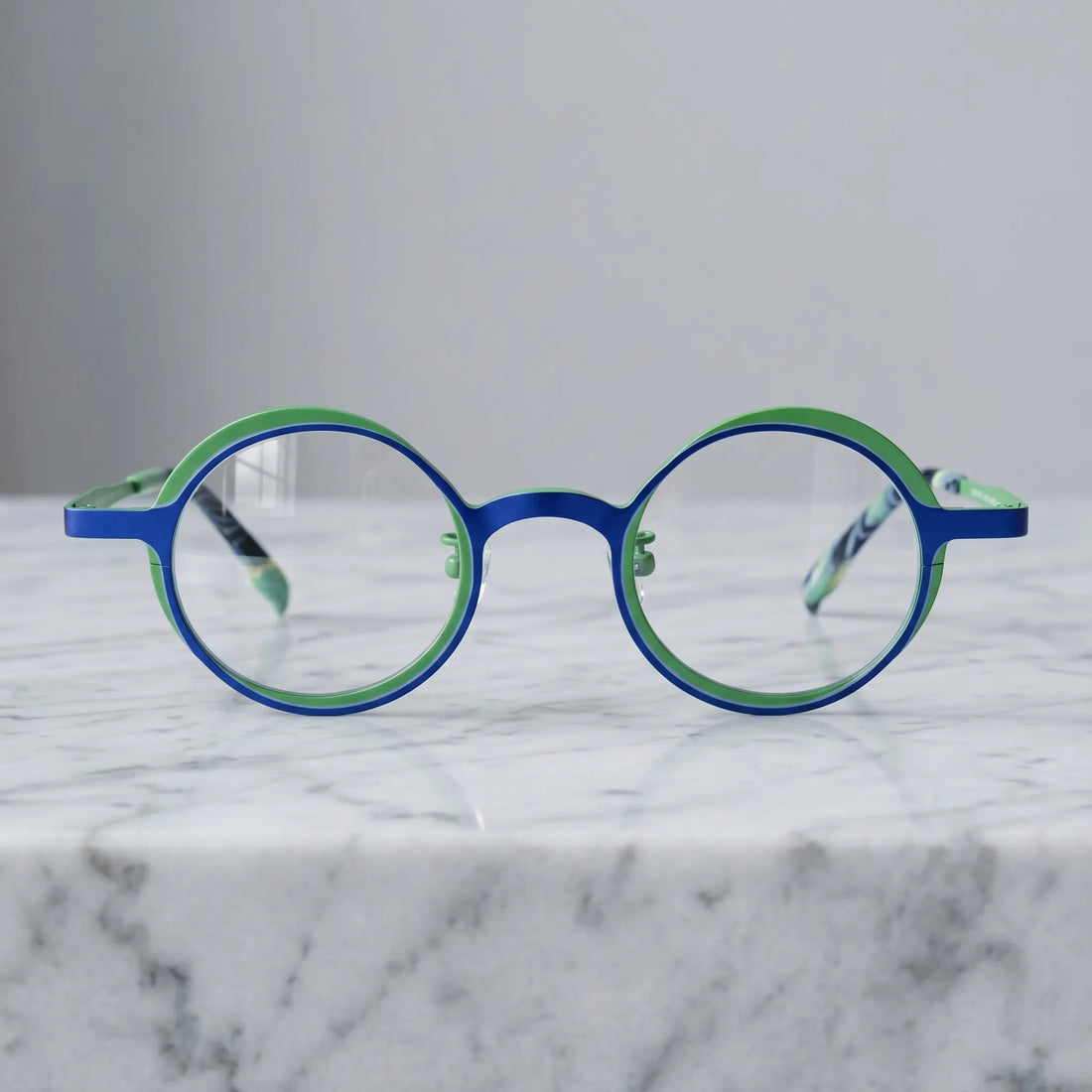 Barledear Cobalt Jade round titanium eyeglasses displayed in a clean lifestyle scene showing the artistic color-block design in vivid cobalt blue and jade green