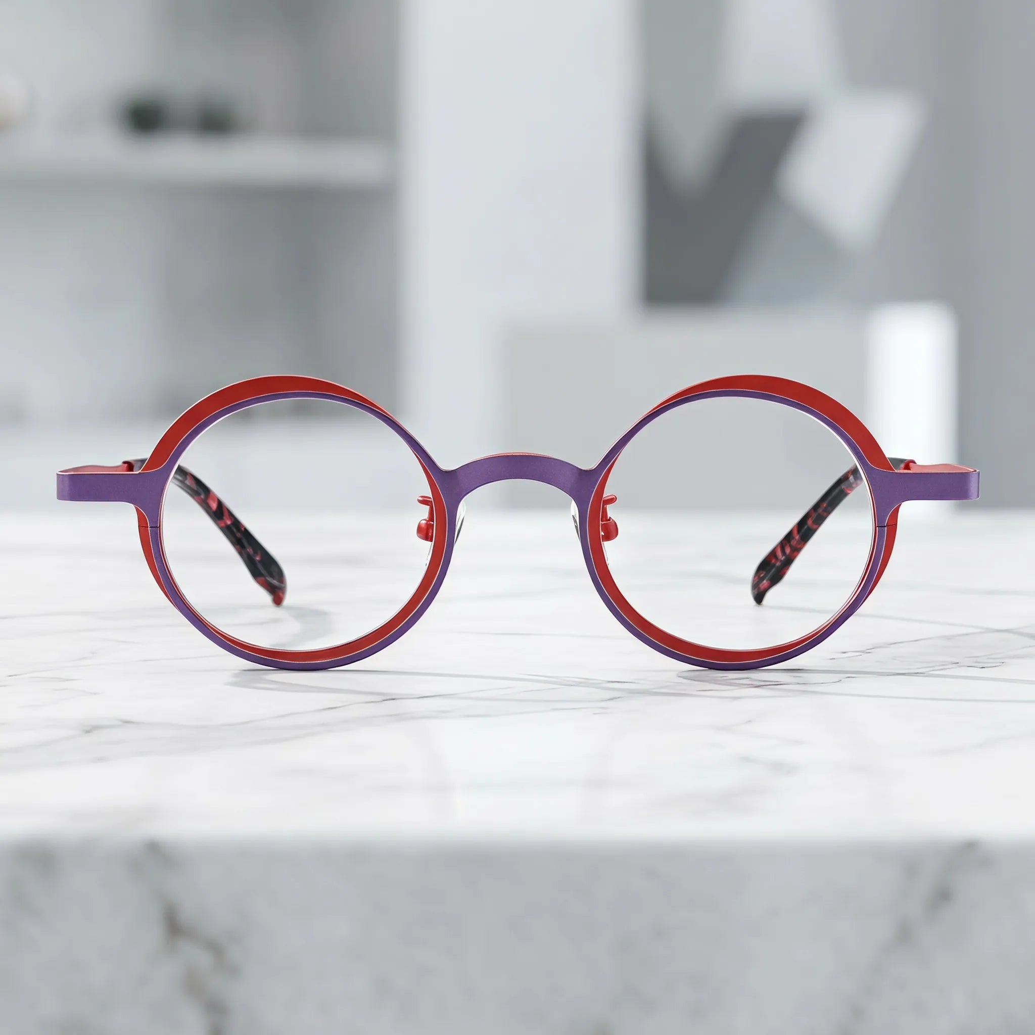 Barledear Crimson Violet round titanium eyeglasses displayed in a clean lifestyle scene showing the artistic color-block design in bold red and violet