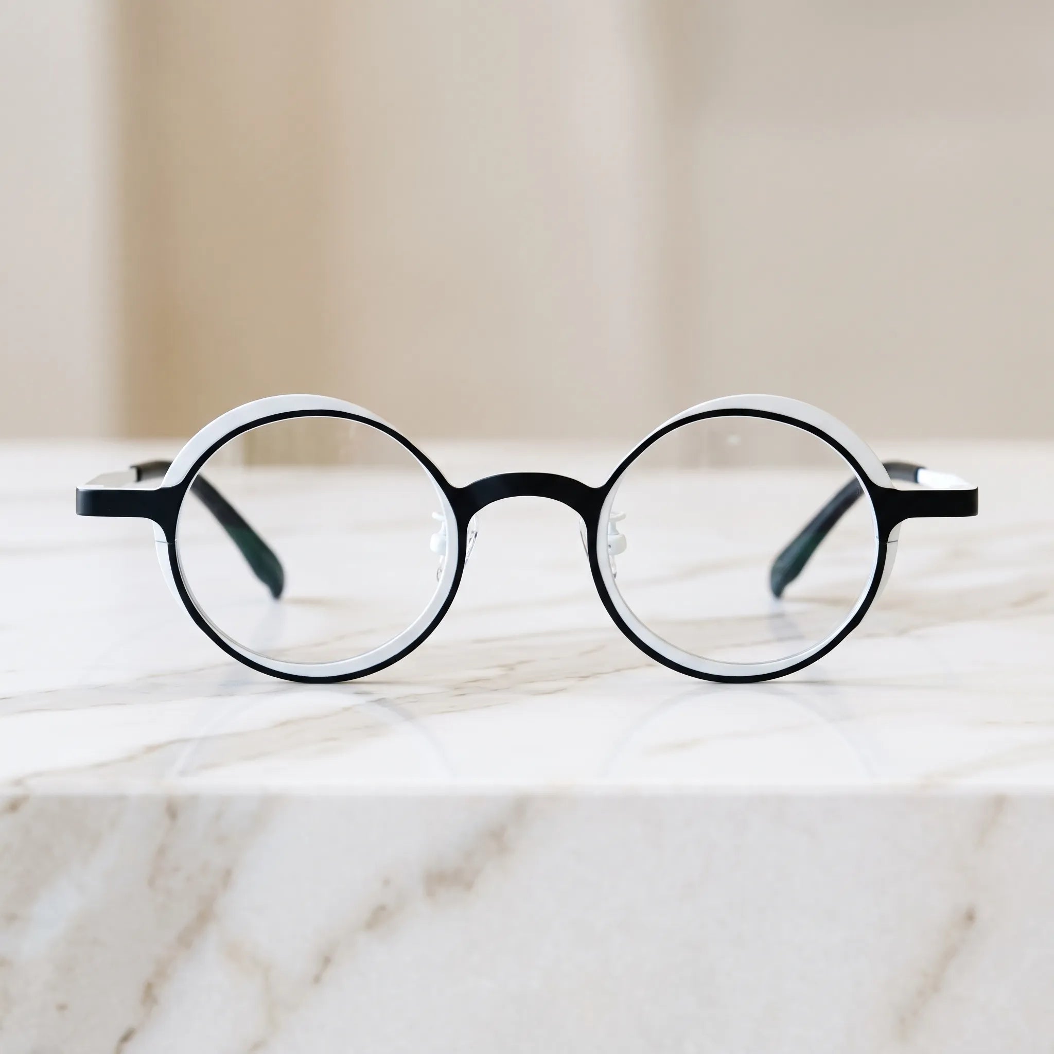 Barledear Onyx Crystal round titanium eyeglasses displayed in a clean lifestyle scene showing the artistic color-block design in clean black and crystal white