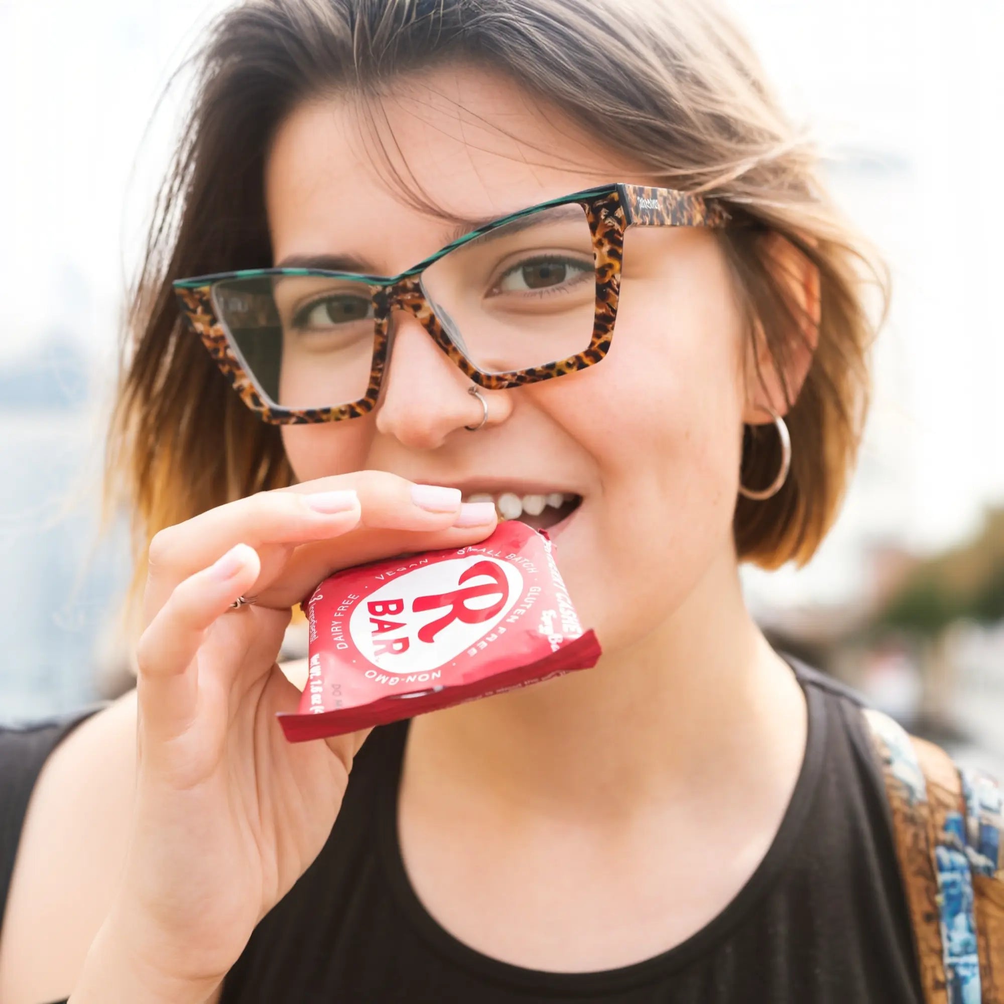 Female model wearing VoyueLens™ emerald tortoise cat-eye glasses, showcasing bold acetate frame in fashion-forward outdoor lifestyle setting