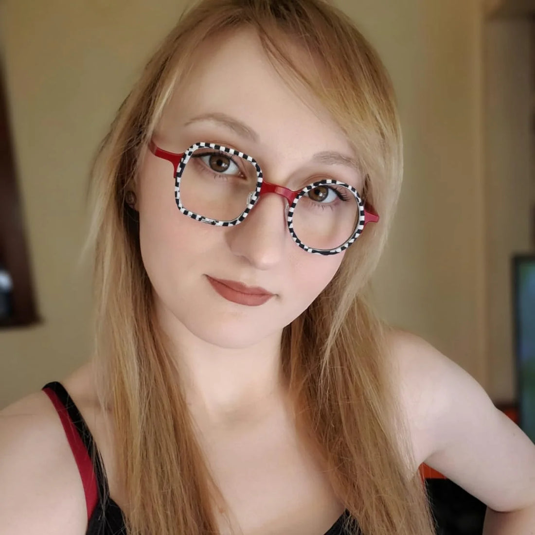 Model wearing VoyueLens Checker Clash Red eyeglasses with bold black and white checker rims and asymmetrical shape, a signature BARLEDEAR design.
