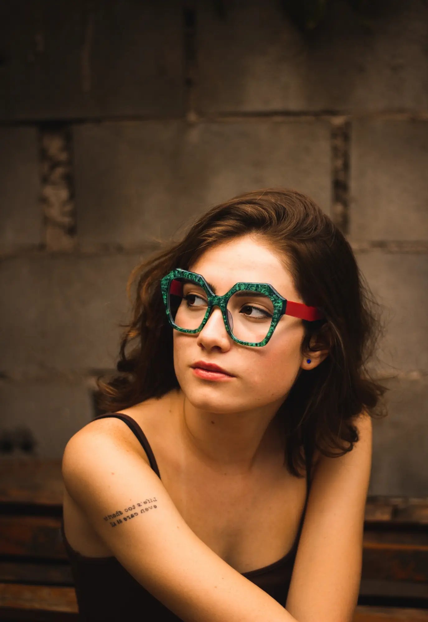 Fashion model wearing VoyueLens Crimson Jade polygon eyeglasses in a natural outdoor scene.