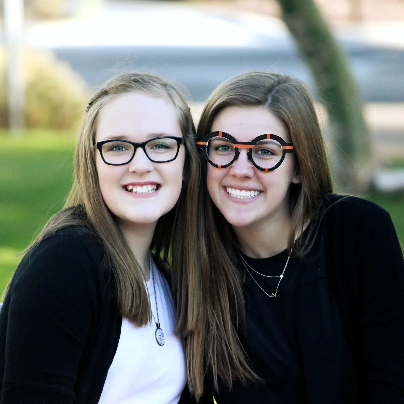Two young girls model showcasing VoyueLens™ glasses in charcoal black with a modern matte texture.