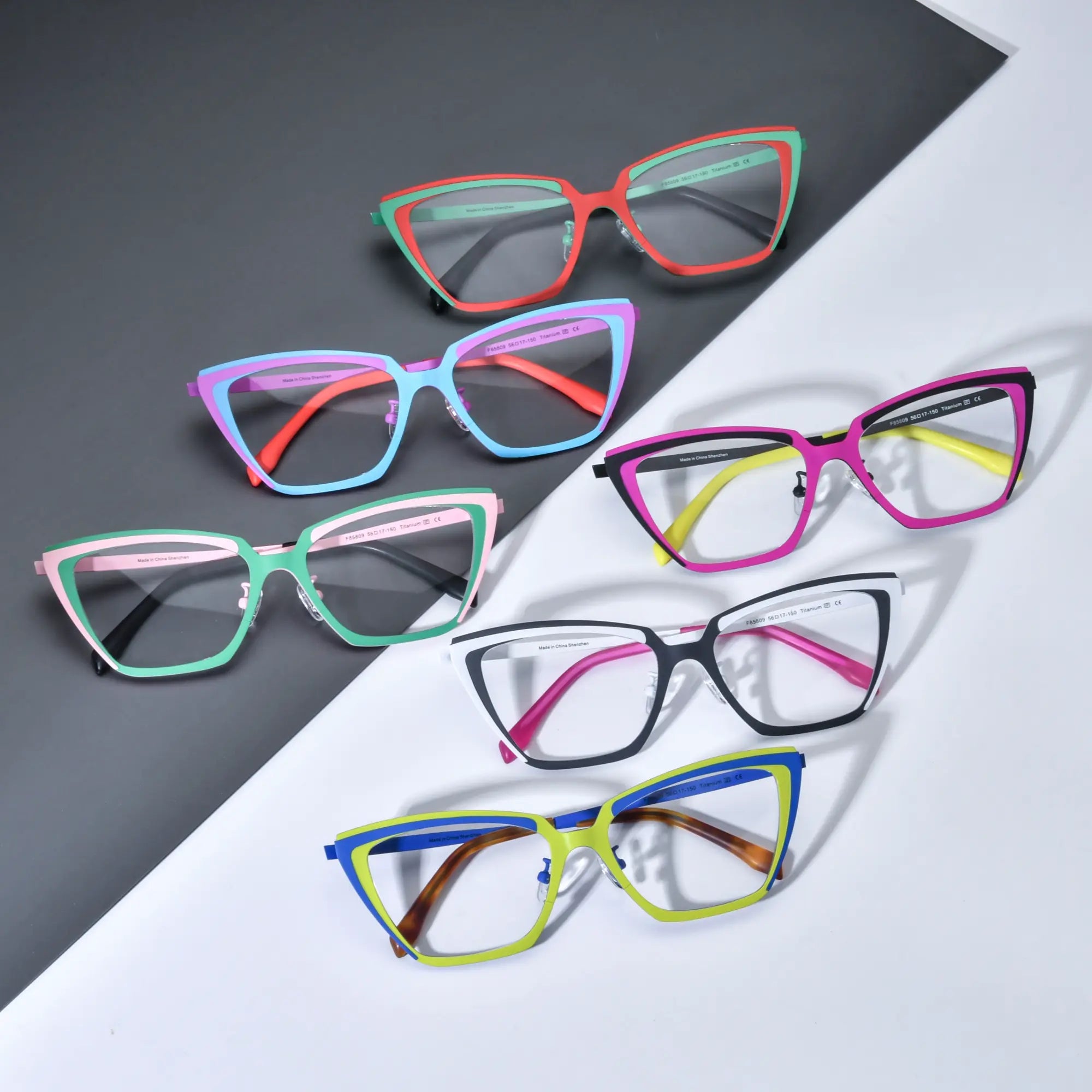 Group shot of VoyueLens™ VL185809 cat-eye titanium glasses in six dual-tone color options, showcasing bold geometric frames on a black and white background.