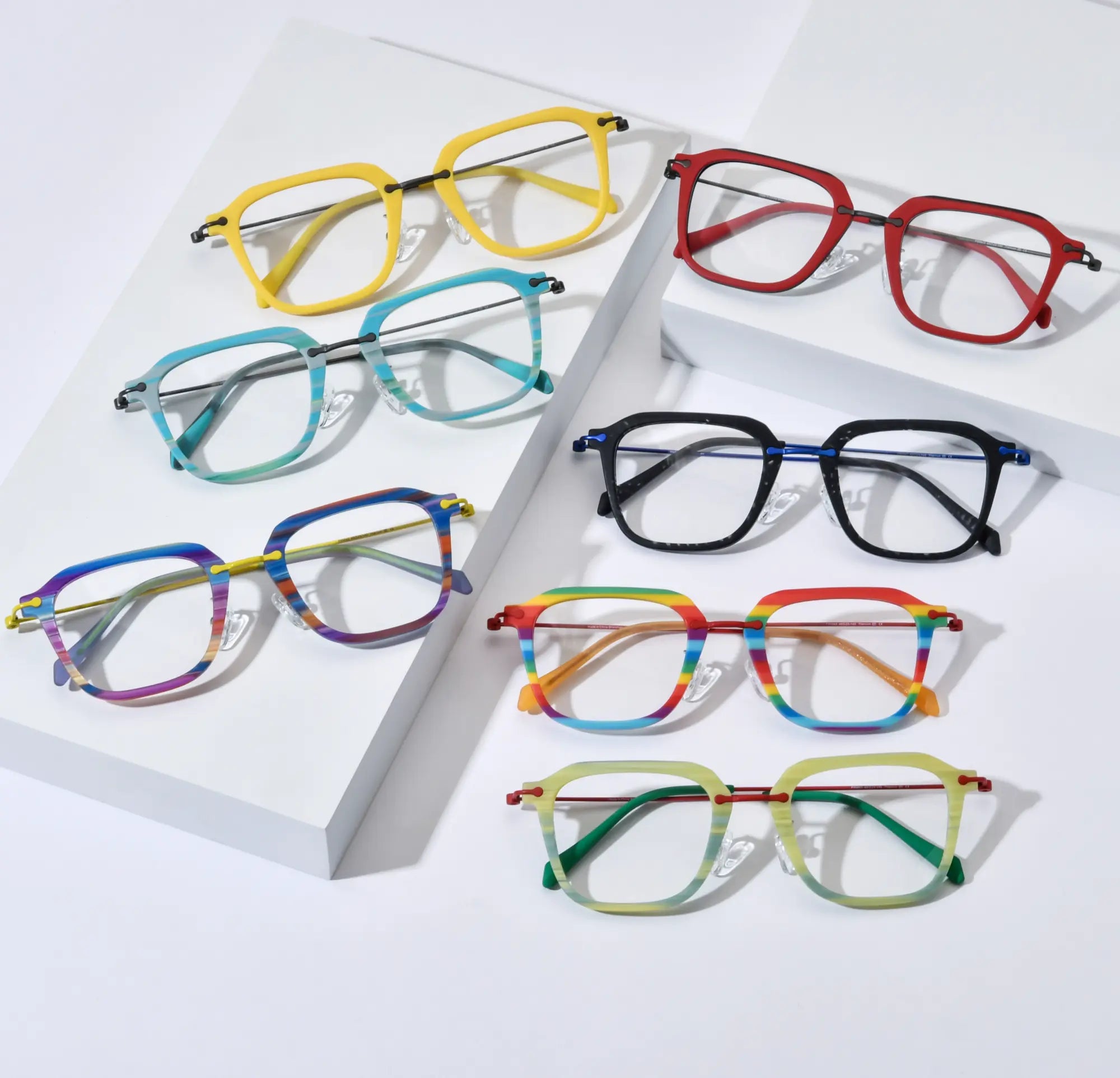 Stylish flat lay composition showcasing the full color range of VoyueLens™ VL185843 Urban Vision eyeglasses. Includes all seven vibrant variants: Sunshine Yellow, Crimson Alloy, Glacier Teal, Midnight Graphite, Vivid Violet Stripe, Rainbow Parade, and Citrus Mist — arranged aesthetically on staggered white platforms, highlighting the modern square design and titanium detailing.