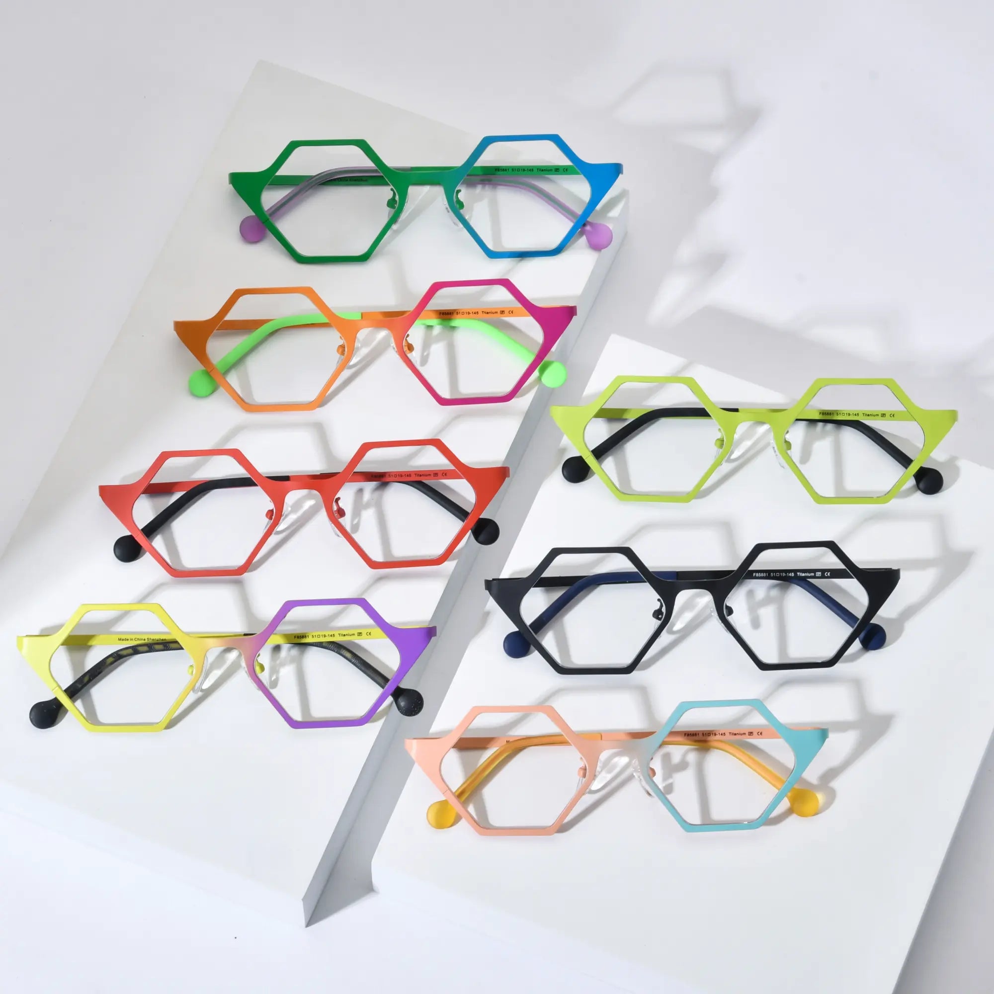 VoyueLens™ VL185881 eyeglasses collection in seven colors displayed on white background – showcasing polygon titanium frames in green-blue, orange-pink, red, yellow-purple, green, black, and pink-cyan.