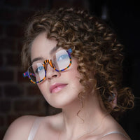 Woman wearing VoyueLens™ VL19352 square eyeglasses in Rainbow Stripe color, close-up portrait with curly hair and soft lighting