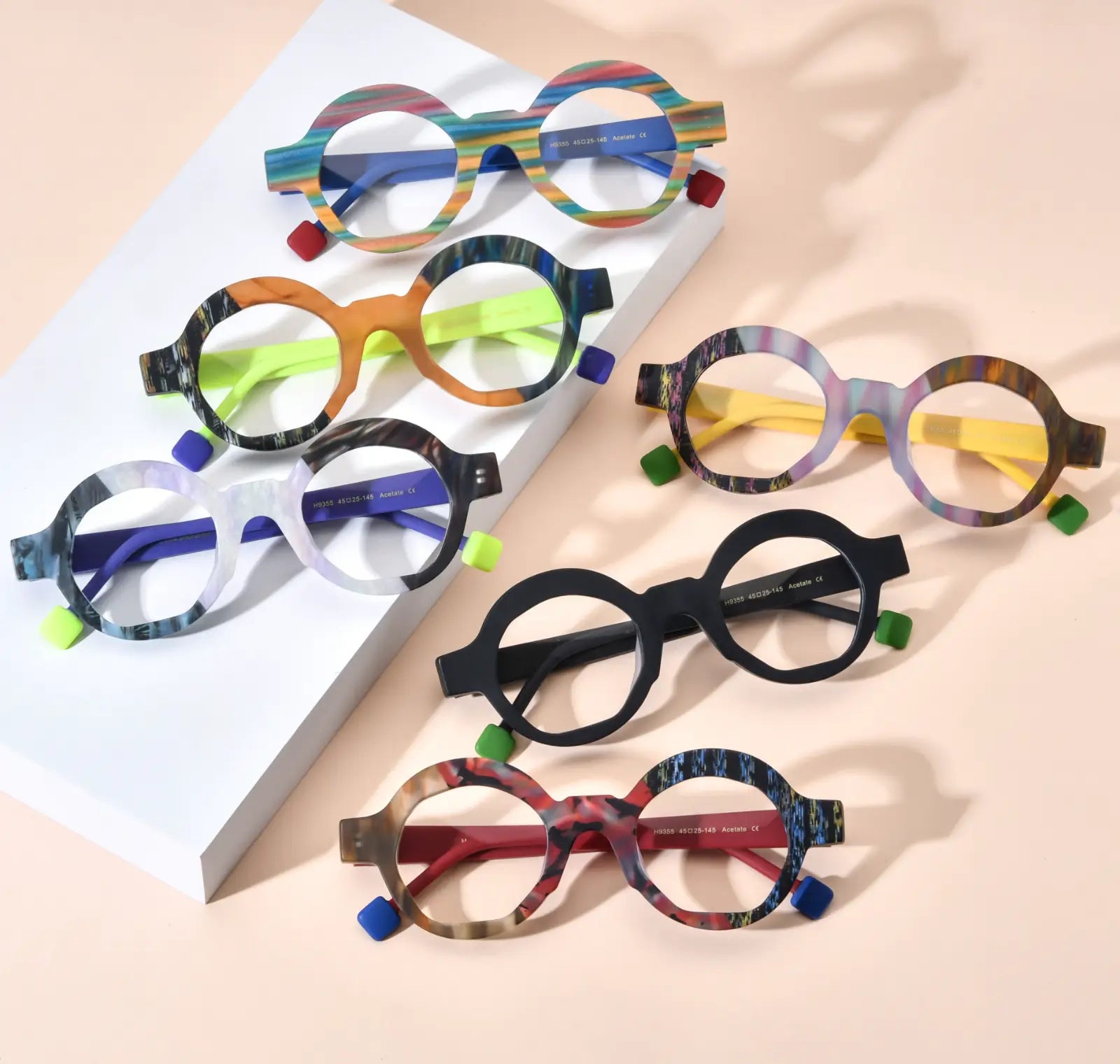 Top-down display of VoyueLens™ VL19355 polygon eyeglasses in all six color variants including Rainbow Stripe, Lime Tortoiseshell, Ice Marble, Aurora Fade, Charcoal Black, and Crimson Nebula, featuring matte acetate frames with contrasting temples, ideal for lightweight prescription eyewear.