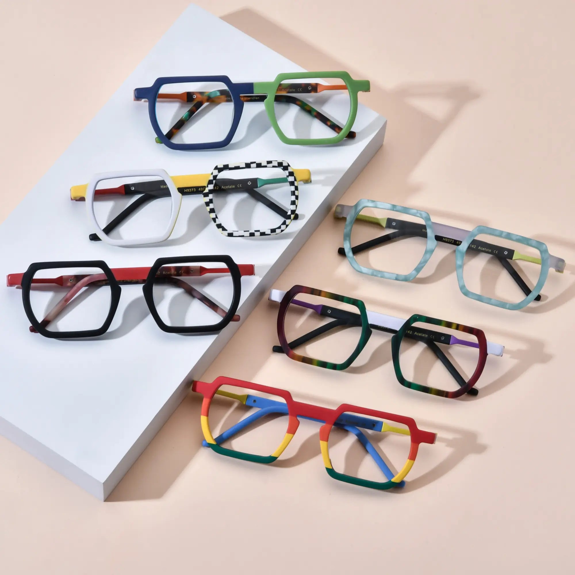 Full product lineup display of VoyueLens™ VL19373 Urban Pop Geometric Eyeglasses featuring six vibrant color variants – Blue-Green Matte, Checkerboard Yellow, Crimson Noir, Ice Marble, Aurora Fade, and Rainbow Rush – arranged in a stylish flat lay on a pastel background showcasing bold acetate frames and artistic streetwear design.