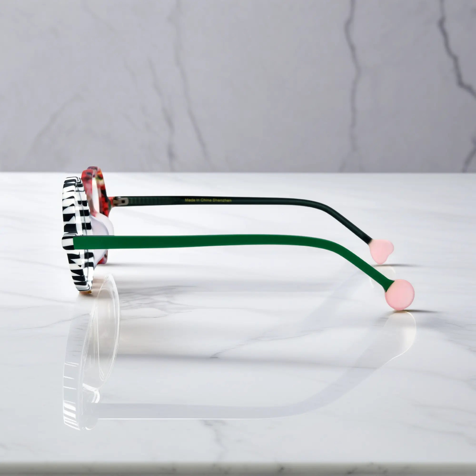 Side profile of Checker Red Pop variant, showcasing frame thickness and temple arm structure. Bold red and black asymmetrical frame with heart and round lenses.