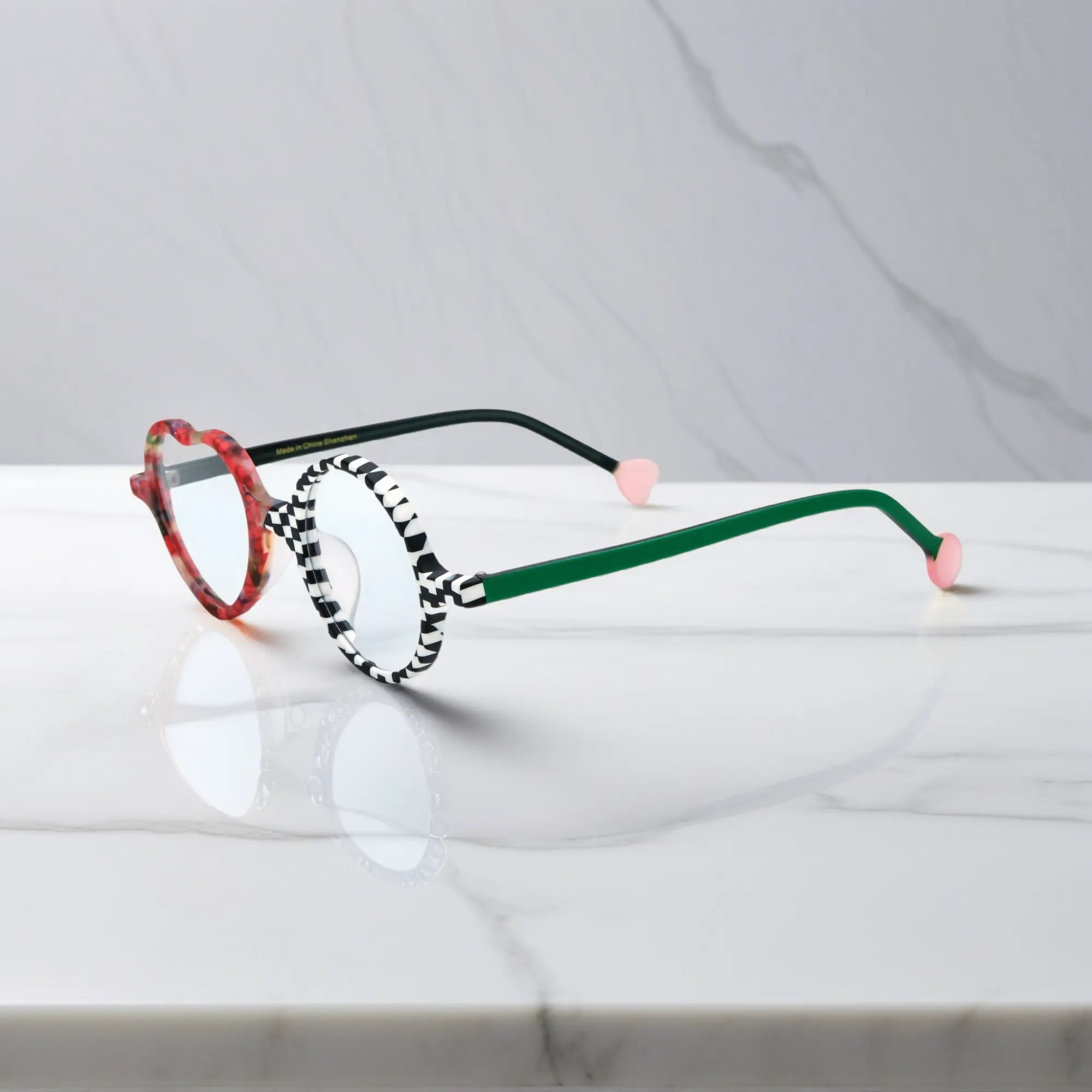 Side view of Checker Red Pop variant, showcasing frame thickness and temple arm structure. Bold red and black asymmetrical frame with heart and round lenses.